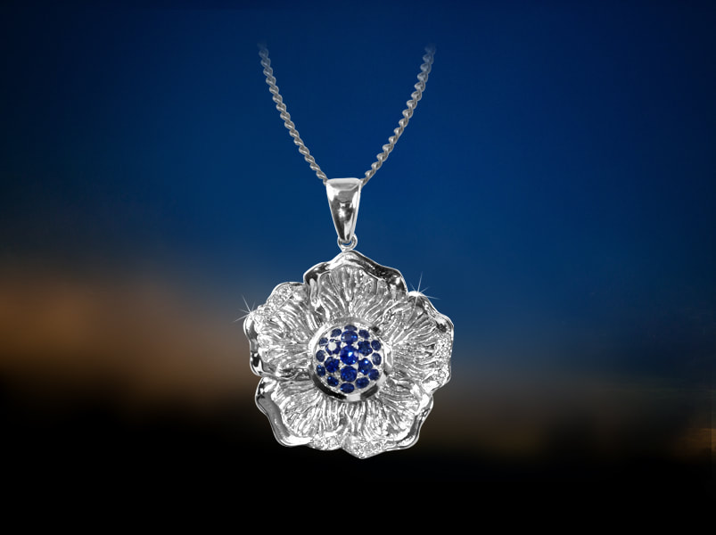 Stylised hibiscus flower pendant in white gold and sapphire center